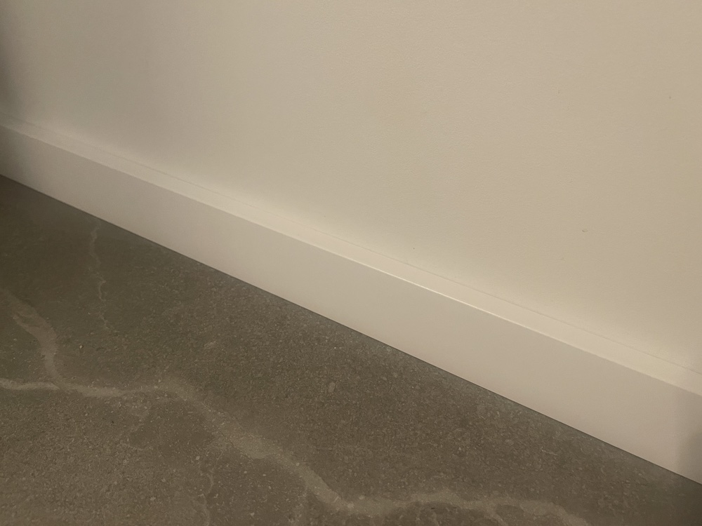 witte plint bij een witte muur en een grijze vloer