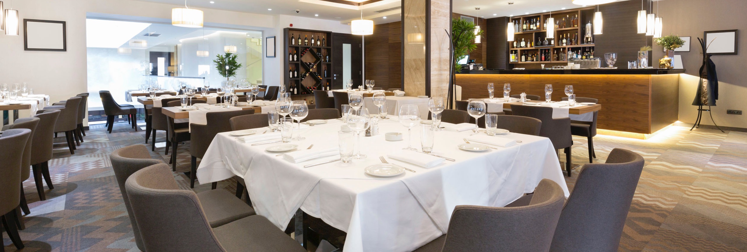 restaurant met bedekte tafels, grijze stoelen en een bar